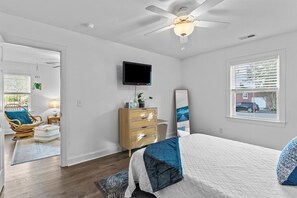 Une chambre à coucher comprenant un lit, un ventilateur de plafond, une télévision, une commode et une fenêtre avec des stores.