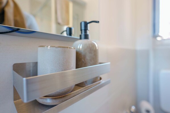 A bathroom shelf with a ceramic mug, a soap dispenser, and a small bowl. - Le Suites dell'Edera (Bologna)
