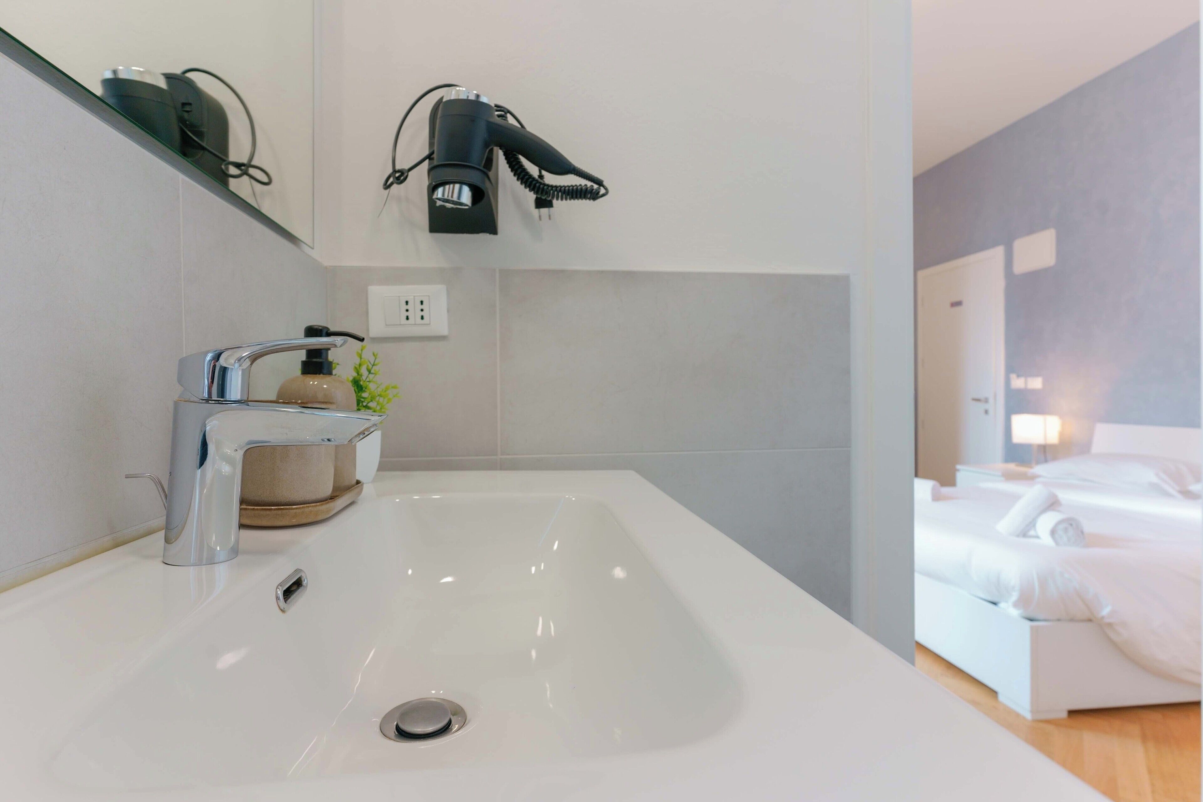 A modern bathroom with a large sink, a hairdryer, and a bottle of soap.
