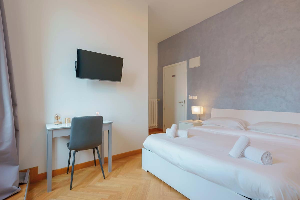 A hotel room with a bed, a desk, a chair, a television, and a bathroom door.