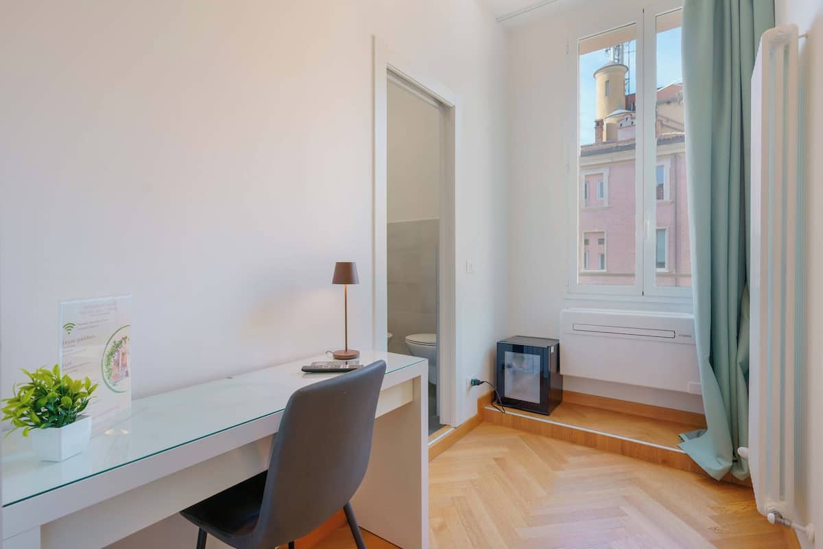 A modern room with a glass desk, a chair, a small plant, a radiator, and a window with curtains.