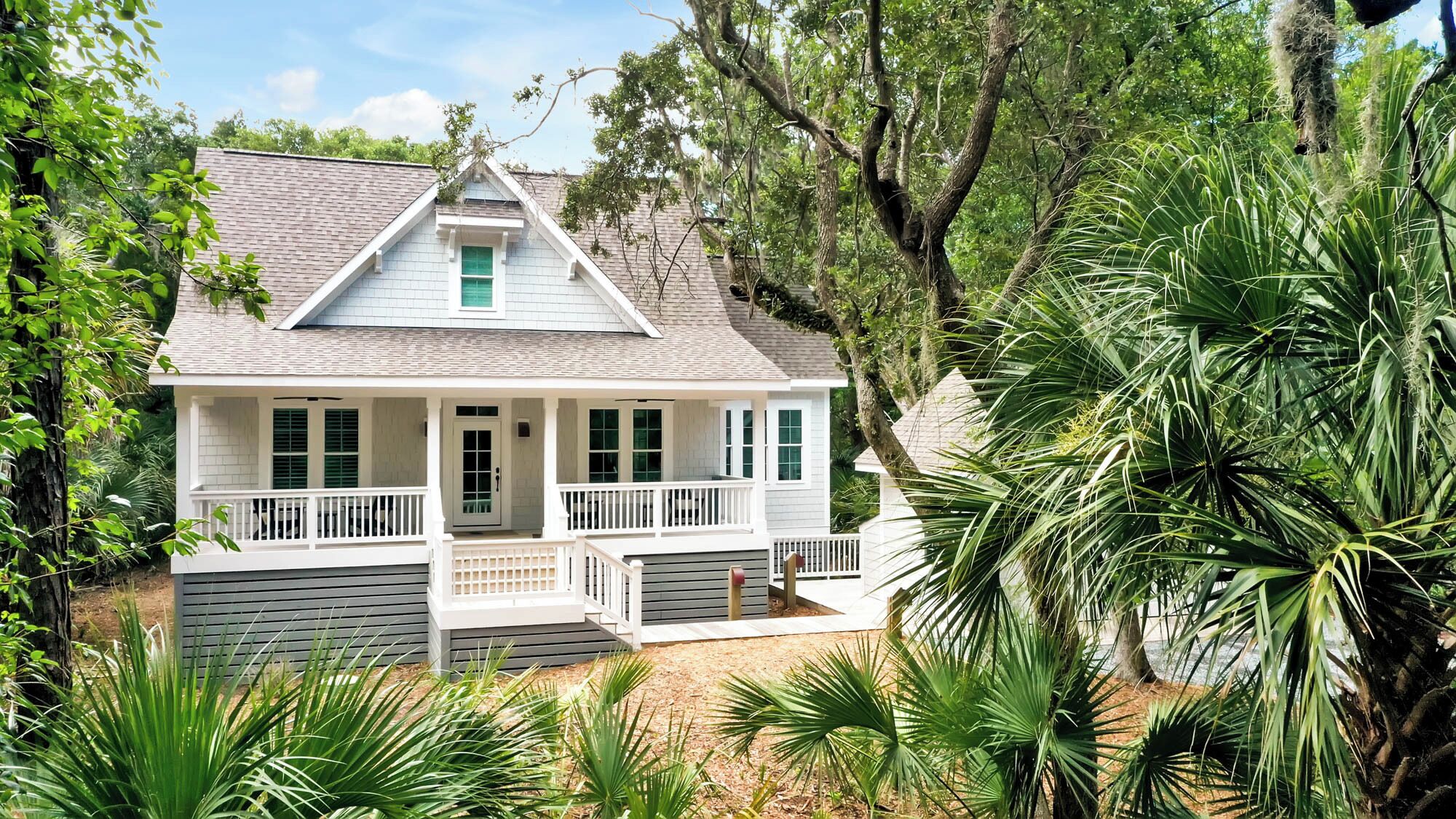 A two-story house with a porch, surrounded by lush greenery and palm trees.