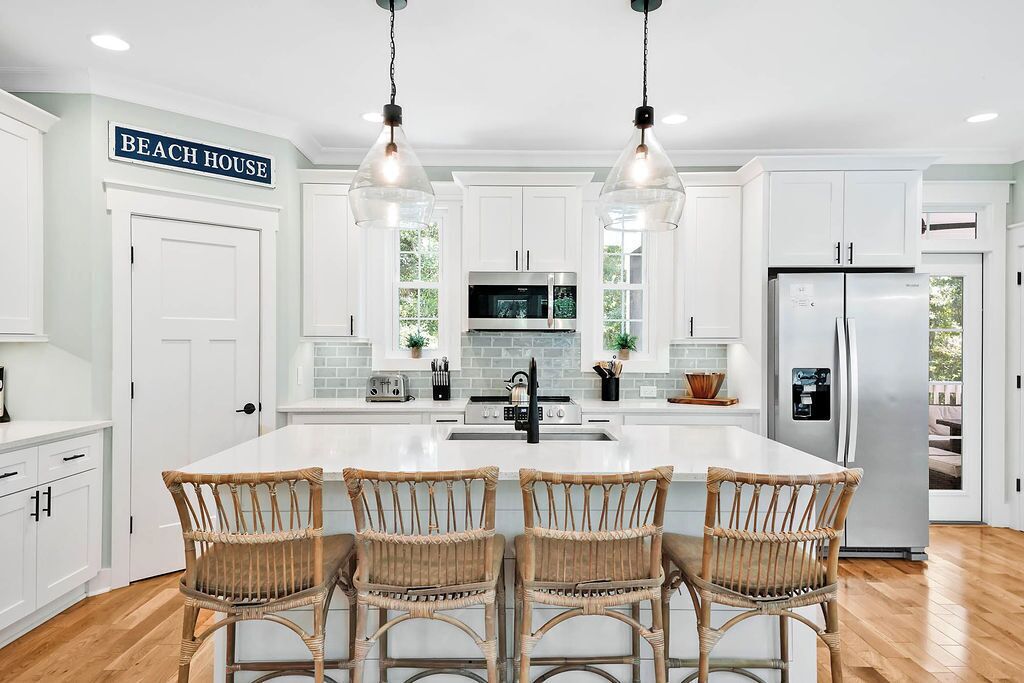 A kitchen with white cabinets, a large island with four wicker chairs, a microwave, and a refrigerator.