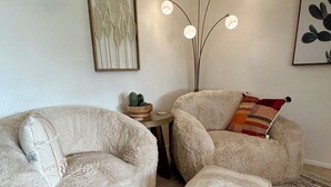 A cozy living room with two plush armchairs, a round ottoman, a patterned rug, a small side table with a cactus, and a floor lamp. - Charming Mesa Golf Course Home (Mesa)