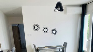 Una sala de estar moderna con un sofá gris, una mesa de centro y una mesa de comedor con sillas. Hay obras de arte decorativas sobre la mesa de comedor.