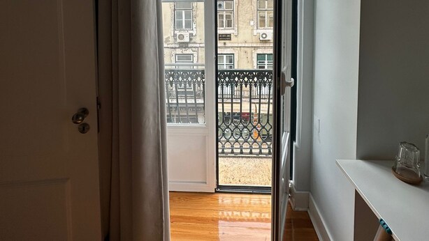 Un couloir mène à un balcon d’où l’on peut admirer un immeuble doté de nombreuses fenêtres et d’une rambarde en métal.