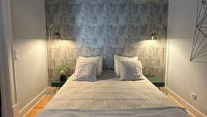 Une chambre avec un mur décoré d’un motif en briques, un lit avec une literie blanche, deux lampes de chevet et une fresque au plafond.