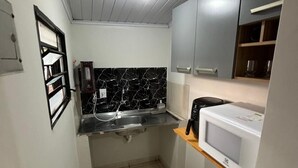 Una cocina compacta con salpicadero de azulejos blanco y negro, un lavamanos de acero inoxidable y un microondas blanco.