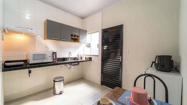 Una cocina moderna con armarios blancos, microondas, cafetera y cubo de basura.