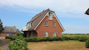 A red brick house with a sloped roof and a balcony. - Ferienwohnung fur 4 in St. Peter-ording (St. Peter-Ording)