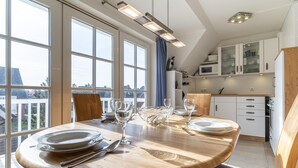 A modern kitchen with large windows, a dining table set with plates and glasses, and a view of the city. - Ferienwohnung fur 4 in St. Peter-ording (St. Peter-Ording)