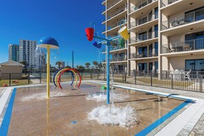 A water play area with a pool, surrounded by a fence, and a multi-story building in the background. - Gulf Coast Paradise Phoenix X 102 (Orange Beach)