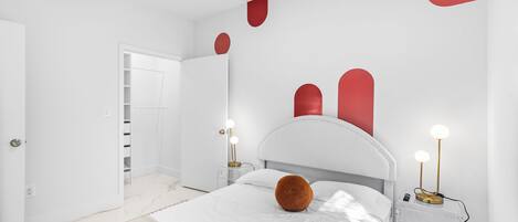 A modern bedroom with a white bed, a clear bedside table, and a nightstand with a lamp.