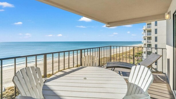 A balcony with a view of the beach and ocean, featuring a table and chairs.