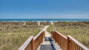 A wooden boardwalk leading to a beach with a clear view of the ocean.