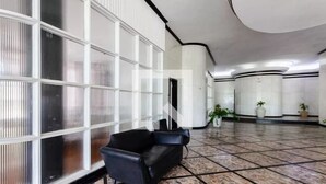 A spacious lobby with a black leather sofa, a large glass wall with vertical blinds, and a tiled floor. - Boqueirão studio apartment in Santos, building facing the beach with partial view (Boqueirão Santos)