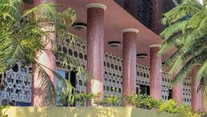 A building with multiple columns, a covered walkway, and surrounding greenery. - Boqueirão studio apartment in Santos, building facing the beach with partial view (Boqueirão Santos)