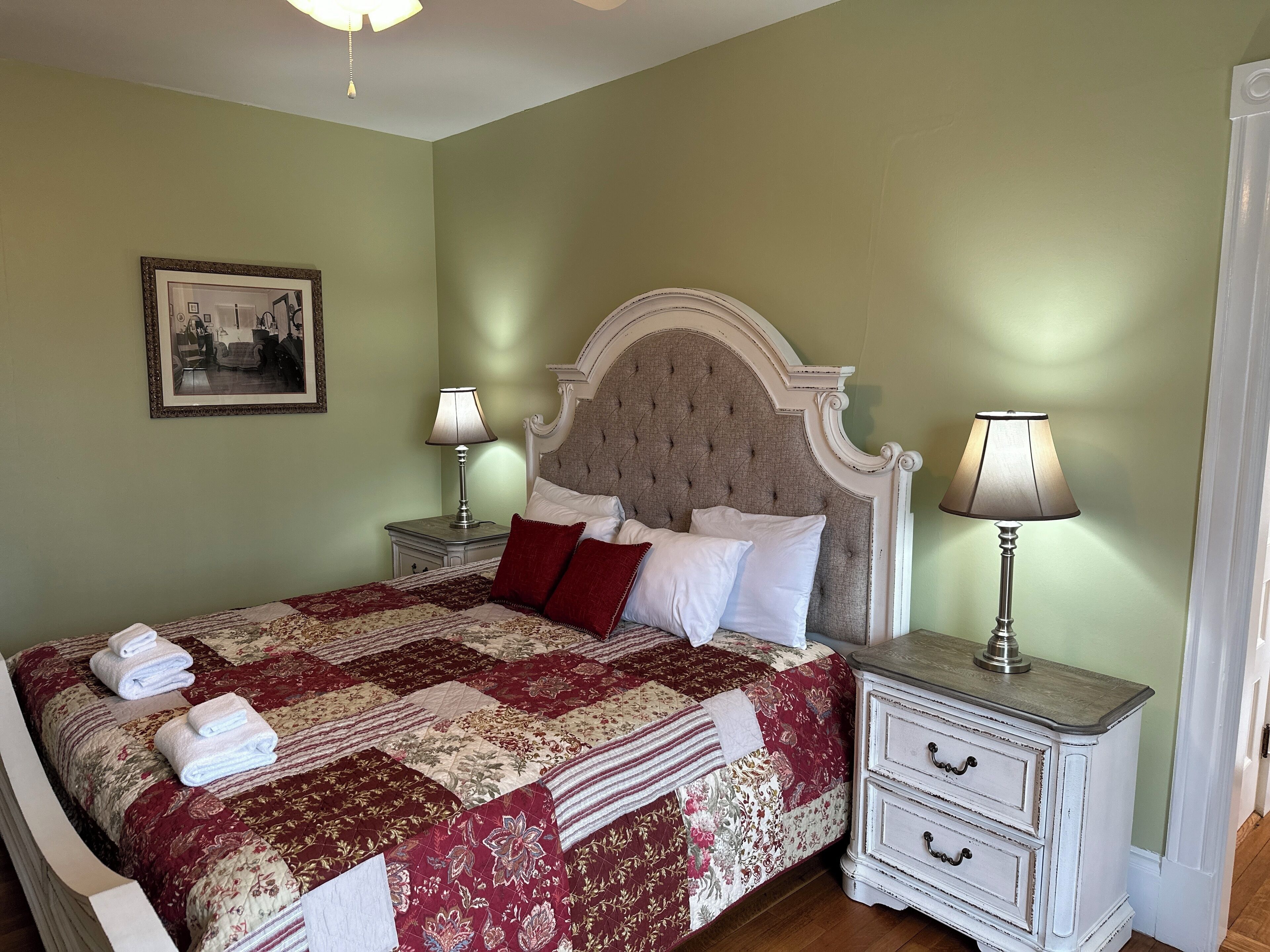 A neatly made bed with a patterned quilt and pillows, two bedside tables with lamps, and a framed picture on the wall.