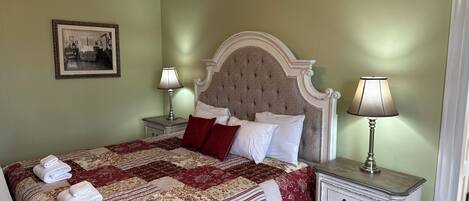 A neatly made bed with a patterned quilt and pillows, two bedside tables with lamps, and a framed picture on the wall.