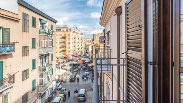 A narrow street with buildings on either side, balconies, and a variety of shops and vehicles. - Casa Sant Agata con Terrazza by Wonderful Italy (Palermo)