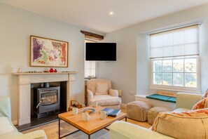 A living room with a fireplace, a sofa, a coffee table, and a television mounted on the wall. - 6 Bed in Lee (oc-d30327) (Ilfracombe)