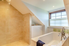 A bathroom with a bathtub, shower, and a window with blinds.