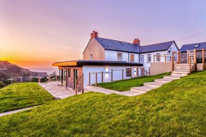 A modern house with a large patio, a staircase, and a view of the ocean at sunset.