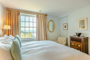 A hotel room with a large bed, a chair, a dresser, a mirror, and a window with curtains. - 6 Bed in Lee (oc-d30327) (Ilfracombe)