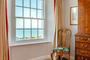 A room with a large window overlooking the sea, a wooden chair with a cushion, and a wooden dresser with drawers. - 6 Bed in Lee (oc-d30327) (Ilfracombe)