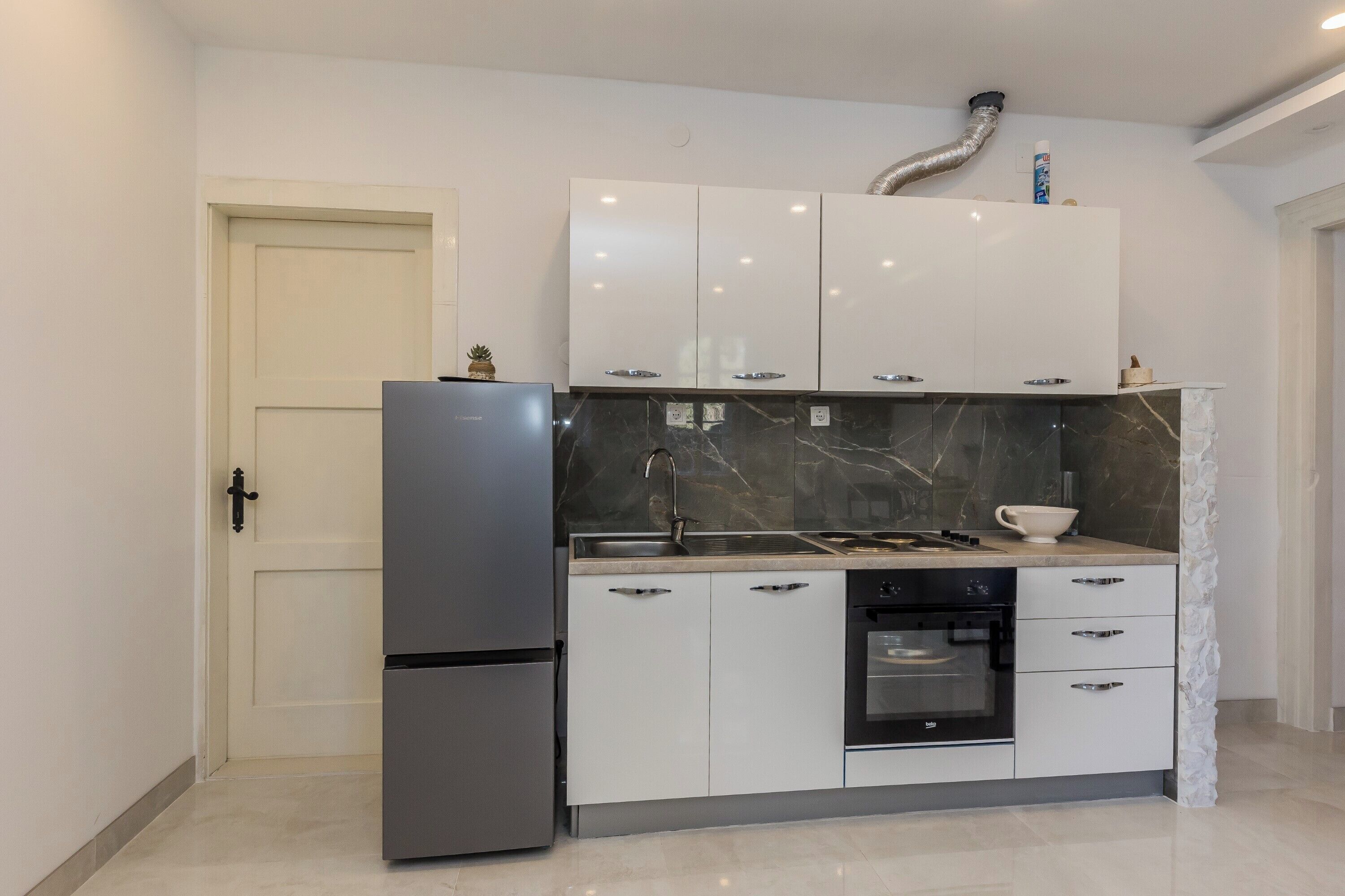 A modern kitchen with white cabinets, a stainless steel refrigerator, a built-in oven, and a marble backsplash.