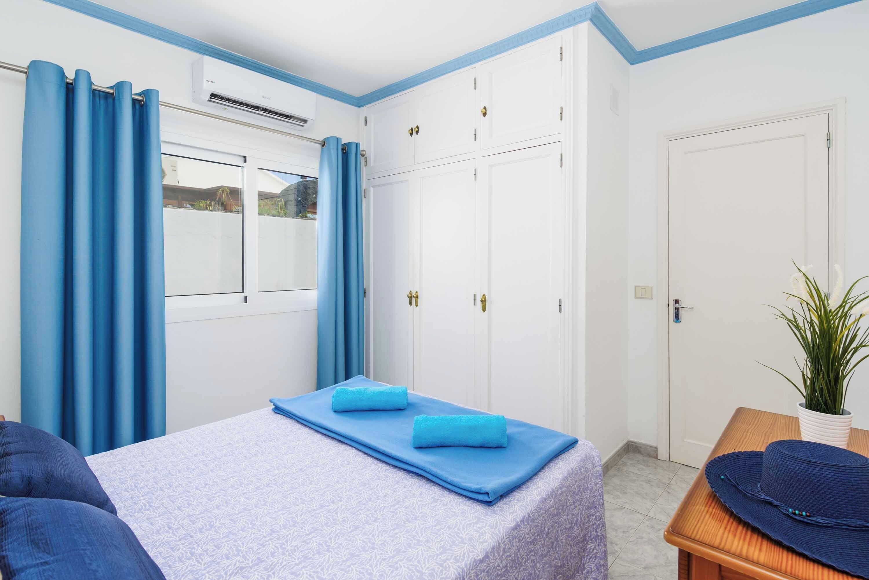 Une chambre à coucher avec un lit, des rideaux bleus, une armoire et une plante en pot.
