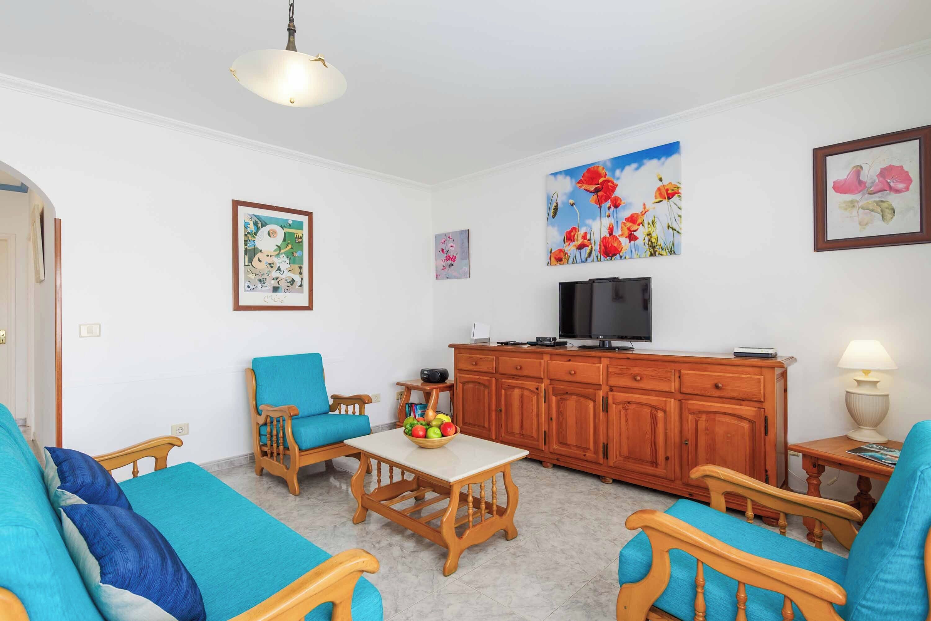 A living room with a sofa, chairs, a TV, wooden cabinets, and artwork on the walls.