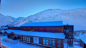 A snow-covered building with a large central hall and smaller rooms, surrounded by mountains. - (1.208) Superbe T2 plein sud aux Ménuires (Les Menuires)