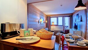 A cozy kitchen with wooden walls, a coffee maker, a basket of bread, and a dining table set for two. - (1.208) Superbe T2 plein sud aux Ménuires (Les Menuires)