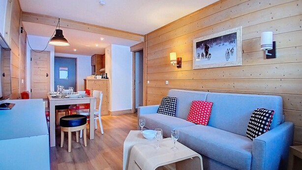 A cozy living room with a sofa, a coffee table, and a dining area with a table and chairs. - (1.208) Superbe T2 plein sud aux Ménuires (Les Menuires)