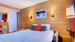 A hotel room with a wooden headboard, a bed with white bedding, two wall-mounted lamps, and a framed picture above the bed. - (1.208) Superbe T2 plein sud aux Ménuires (Les Menuires)