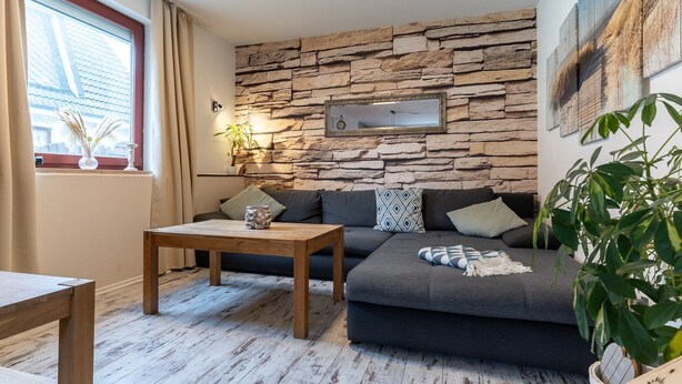 Ett vardagsrum med en vägg av sten, en soffa, ett soffbord och ett fönster med gardiner.