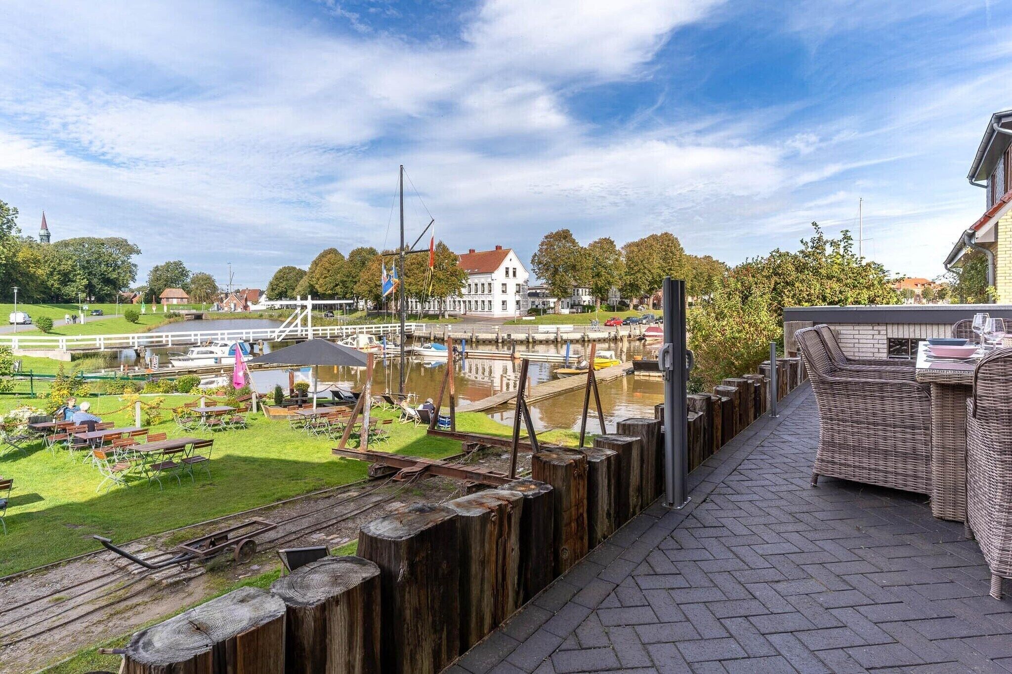 A riverside view with a dining area, wooden deck, and a white building in the background.