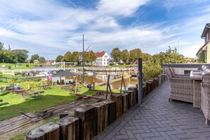 Aussicht auf einen Fluss mit Essbereich, Holzterrasse und einem weißen Gebäude im Hintergrund.