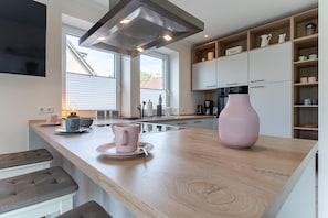 A modern kitchen with a wooden countertop, a large pink vase, and a coffee maker.