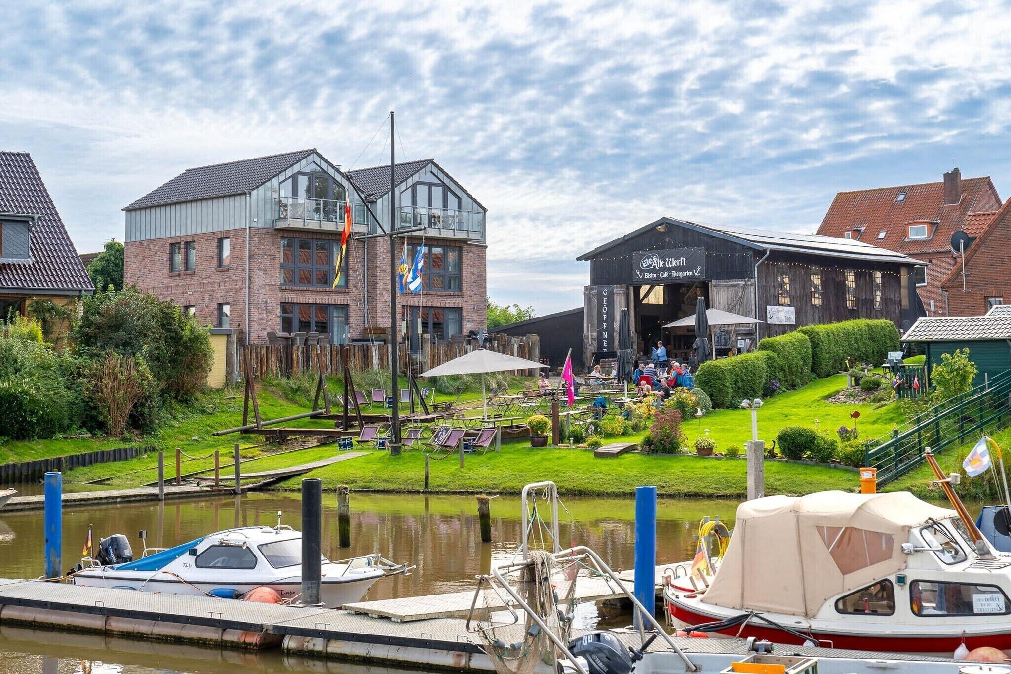 A riverside location with a riverside café, a boat moored at the dock, and a building with a sign for a restaurant.