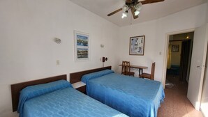 Een kamer met twee bedden, een plafondventilator, een tafel met stoelen en een deur naar een andere kamer.