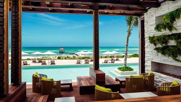Eine Holzterrasse mit Außenmöbeln, einem Pool und Blick auf Strand und Meer.