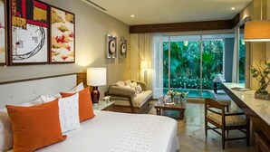 Ein Hotelzimmer mit einem großen Bett, einer Couch, einem Esstisch und Blick auf einen Pool und Grünflächen.