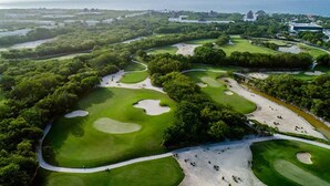 Luftaufnahme eines Golfplatzes mit mehreren Grüns, Sandbunkern und einer Küstenlandschaft im Hintergrund.