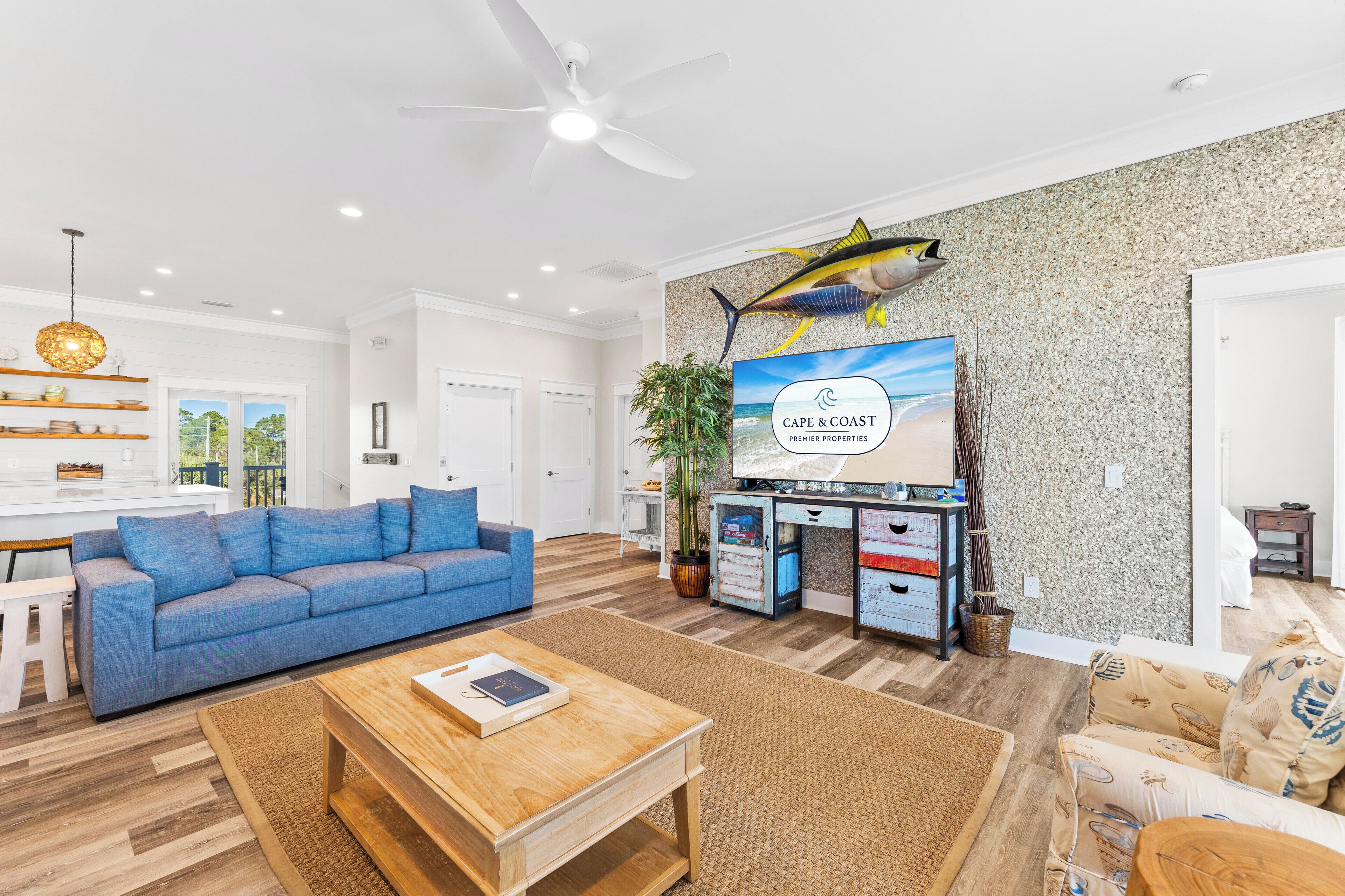 A spacious living room with a blue sofa, wooden coffee table, and a television mounted on the wall.