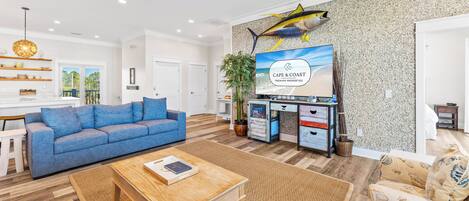 A spacious living room with a blue sofa, wooden coffee table, and a television mounted on the wall.