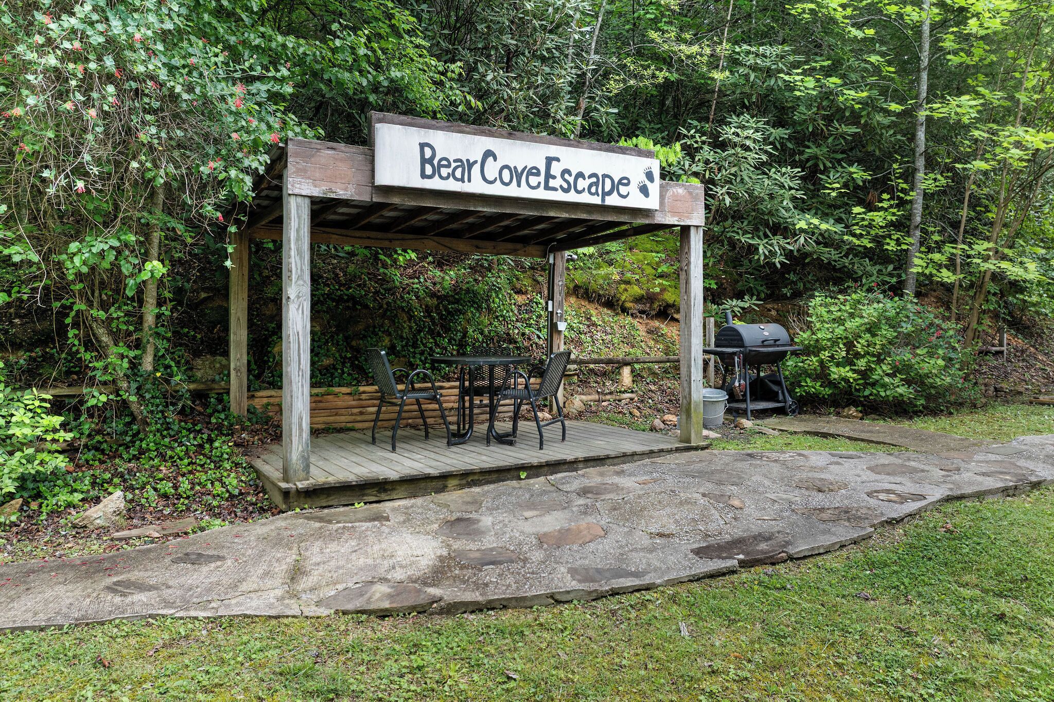 Un pabellón de madera con un cartel que dice "BearCoveEscape" y una parrilla de barbacoa cerca.