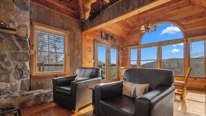 A cozy cabin interior with stone walls, wooden floors, and large windows offering scenic views. - 1 Great Mountain View-3 Bed Cabin in Wears Valley (SEVIERVILLE)