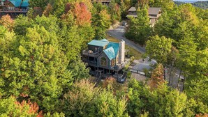 A large, multi-story lodge with a prominent stone chimney, surrounded by dense forest. - 1 Great Mountain View-3 Bed Cabin in Wears Valley (SEVIERVILLE)
